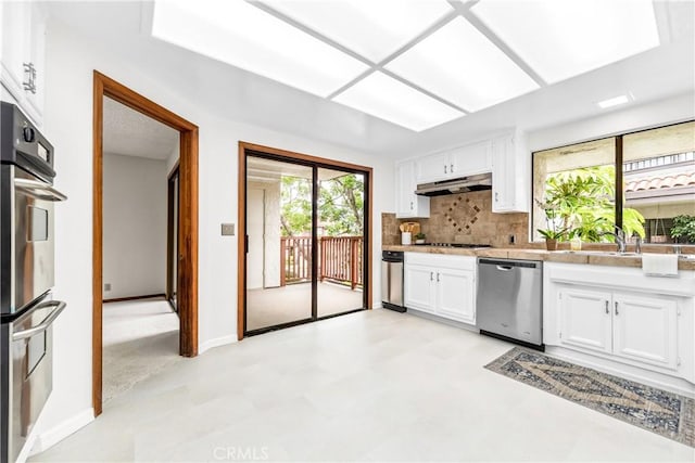 kitchen featuring under cabinet range hood, white cabinetry, light countertops, tasteful backsplash, and appliances with stainless steel finishes