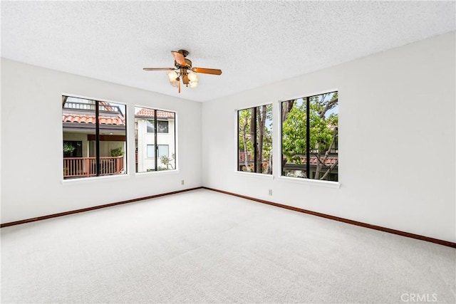 carpeted empty room featuring a textured ceiling, baseboards, a ceiling fan, and a healthy amount of sunlight