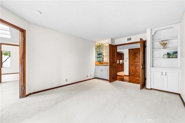 unfurnished bedroom with a textured ceiling, baseboards, a sink, arched walkways, and light colored carpet