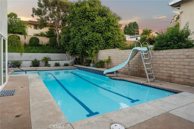 pool at dusk featuring a water slide, a fenced in pool, and a fenced backyard