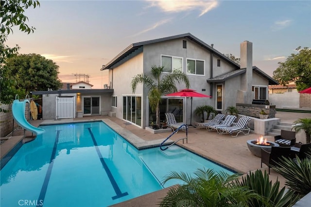 back of house at dusk featuring fence, an outdoor pool, a patio area, stucco siding, and a fire pit