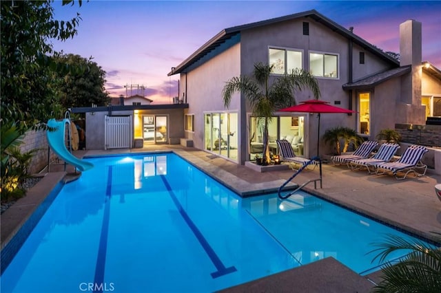 pool at dusk with a patio area, a water slide, and an outdoor pool