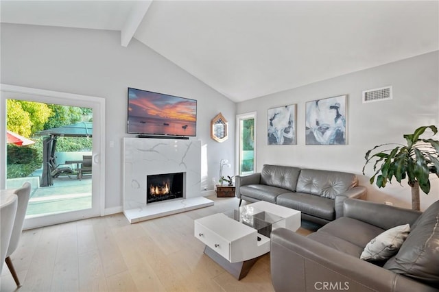 living area featuring light wood-style floors, visible vents, a healthy amount of sunlight, and vaulted ceiling with beams