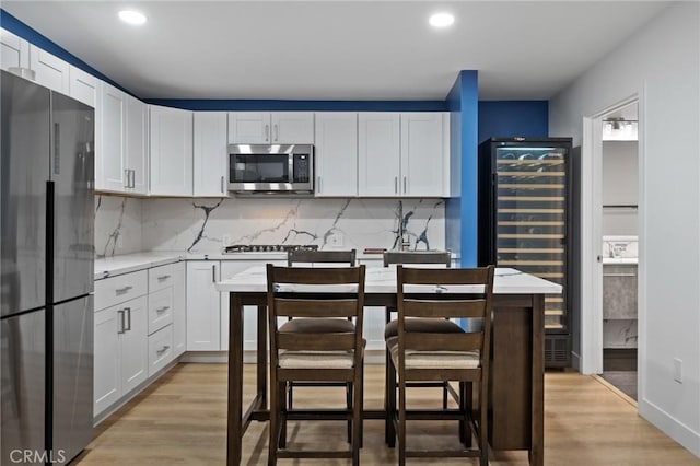 kitchen with wine cooler, light wood-type flooring, appliances with stainless steel finishes, and tasteful backsplash