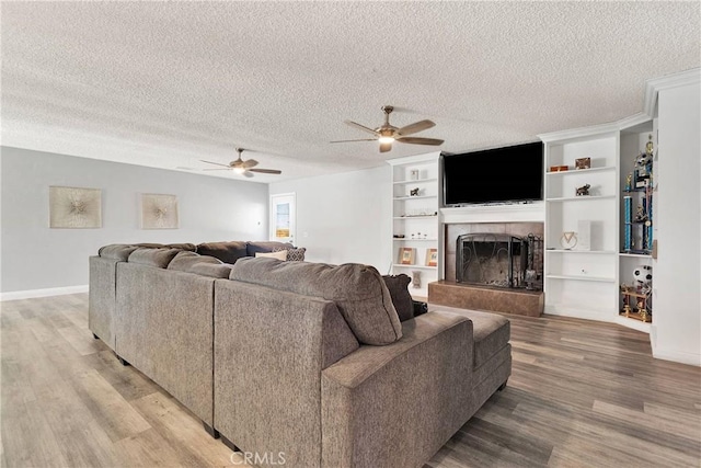 living area with a ceiling fan, a textured ceiling, baseboards, light wood finished floors, and a tile fireplace