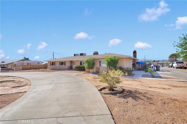 ranch-style home featuring curved driveway, fence, stucco siding, and a chimney