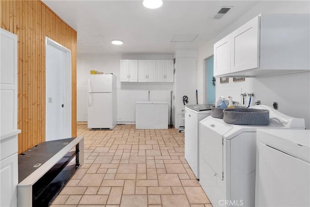 laundry area featuring brick patterned floor, visible vents, wood walls, washing machine and clothes dryer, and cabinet space
