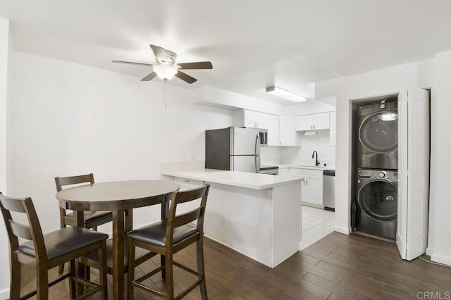 kitchen featuring a peninsula, a ceiling fan, a sink, stacked washer and dryer, and stainless steel appliances