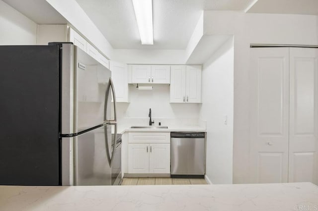 kitchen with a sink, light stone countertops, white cabinets, and appliances with stainless steel finishes