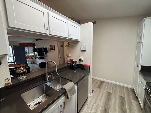 kitchen featuring a sink, appliances with stainless steel finishes, white cabinetry, dark countertops, and light wood-style floors