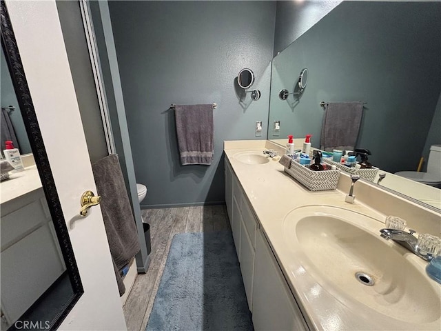 bathroom featuring a sink, double vanity, toilet, and wood finished floors