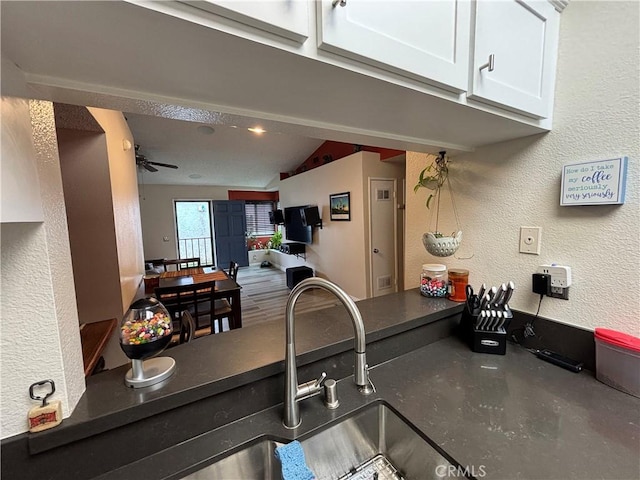 kitchen featuring a sink, lofted ceiling, a textured wall, white cabinets, and dark countertops
