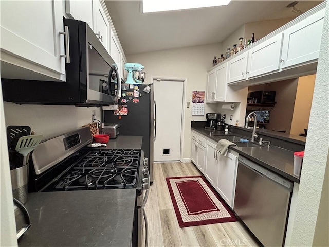 kitchen featuring white cabinets, dark countertops, light wood-type flooring, and stainless steel appliances