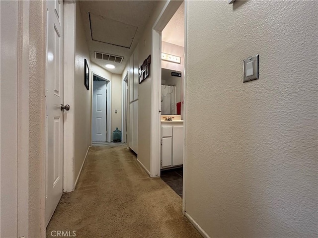 hall featuring carpet flooring, baseboards, a textured wall, and visible vents