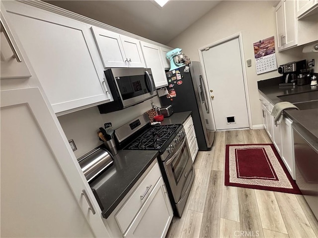 kitchen featuring dark countertops, a sink, light wood-style floors, stainless steel appliances, and white cabinets