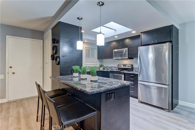 774 Via Los Altos Unit P, Laguna Woods, CA 92637 - kitchen featuring appliances with stainless steel finishes, a skylight, light wood finished floors, a breakfast bar area, and dark stone countertops