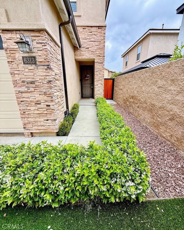 property entrance featuring stone siding, stucco siding, and fence