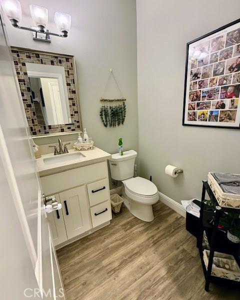 half bathroom with toilet, baseboards, vanity, and wood finished floors
