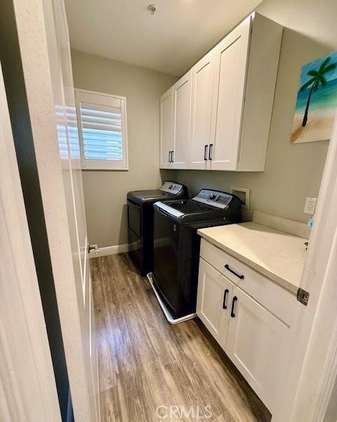 washroom with baseboards, light wood-style floors, independent washer and dryer, and cabinet space