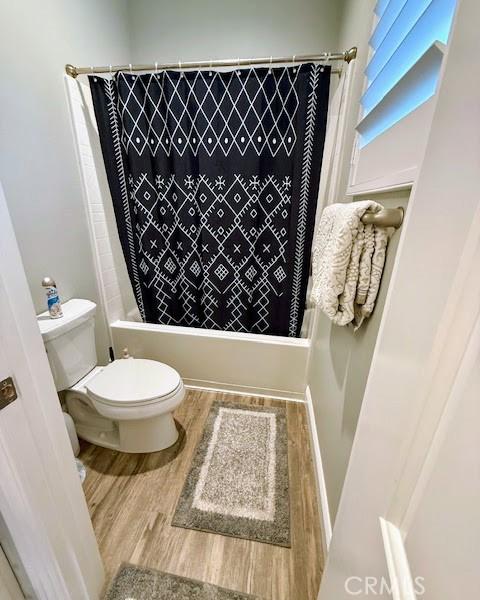 full bath with toilet, shower / bath combo with shower curtain, and wood finished floors