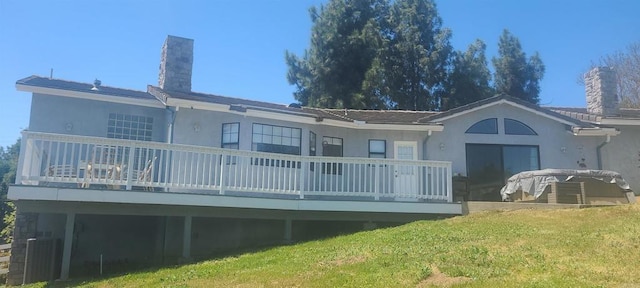 back of property with a chimney, a deck, stucco siding, and a lawn