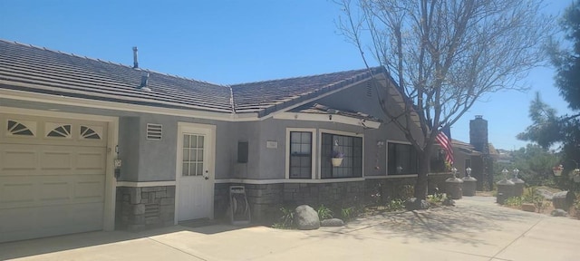 view of front of property featuring stone siding, an attached garage, stucco siding, a tile roof, and concrete driveway