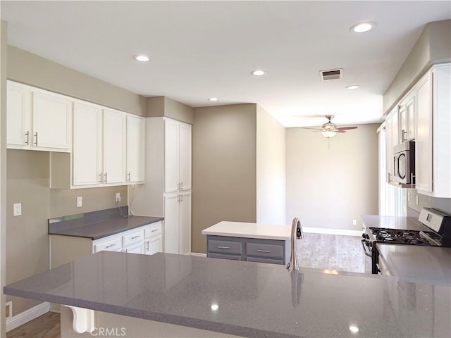kitchen with wood finished floors, dark stone counters, stainless steel appliances, white cabinetry, and visible vents