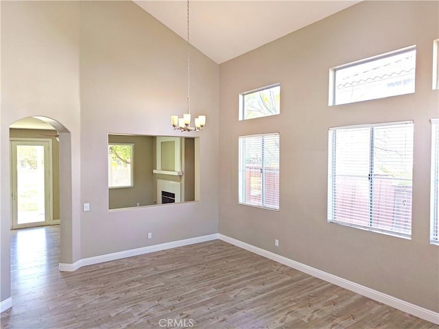 empty room featuring baseboards, a chandelier, high vaulted ceiling, wood finished floors, and arched walkways