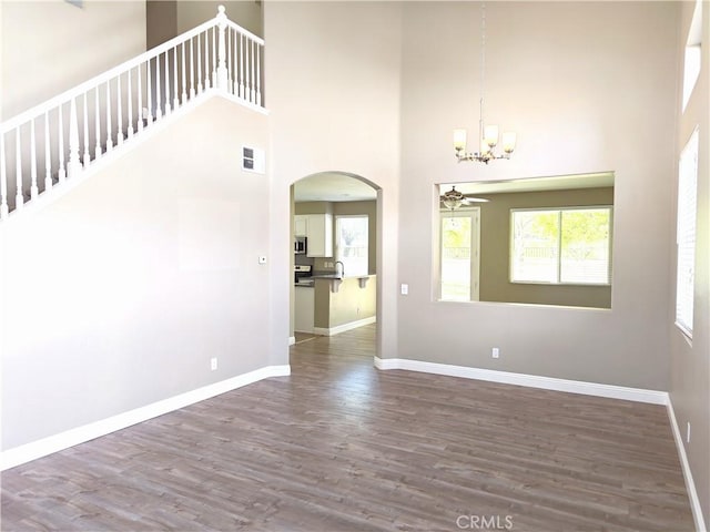 unfurnished living room with baseboards, visible vents, wood finished floors, arched walkways, and a high ceiling