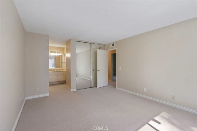 unfurnished bedroom featuring ensuite bathroom, a closet, light colored carpet, visible vents, and baseboards