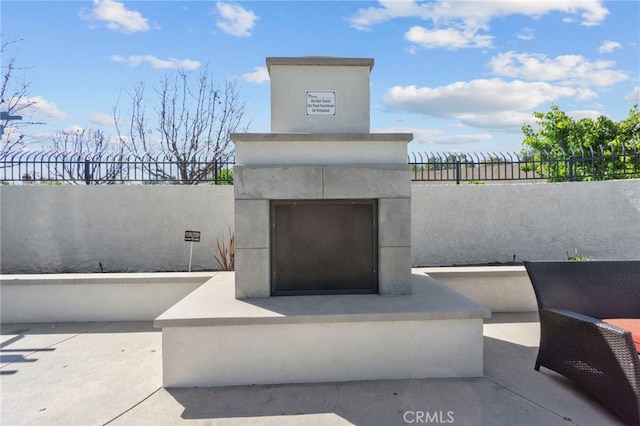 exterior space with an outdoor fireplace, a patio, stucco siding, and fence