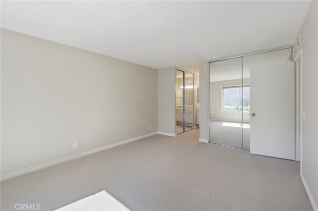 unfurnished bedroom with baseboards, ensuite bathroom, light carpet, and visible vents