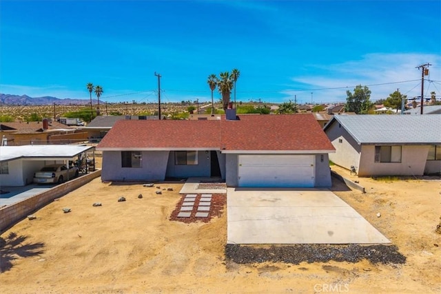 ranch-style house with an attached garage, stucco siding, a mountain view, and driveway