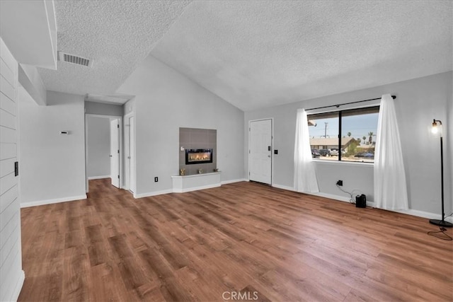 unfurnished living room with a textured ceiling, a glass covered fireplace, visible vents, vaulted ceiling, and wood finished floors