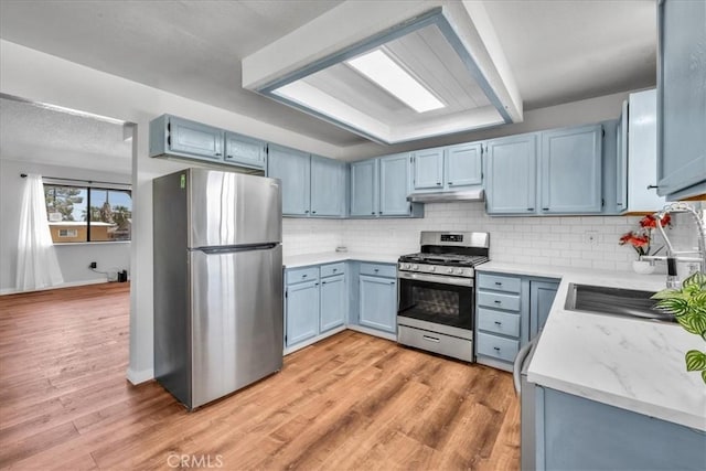 kitchen featuring under cabinet range hood, blue cabinets, backsplash, and appliances with stainless steel finishes