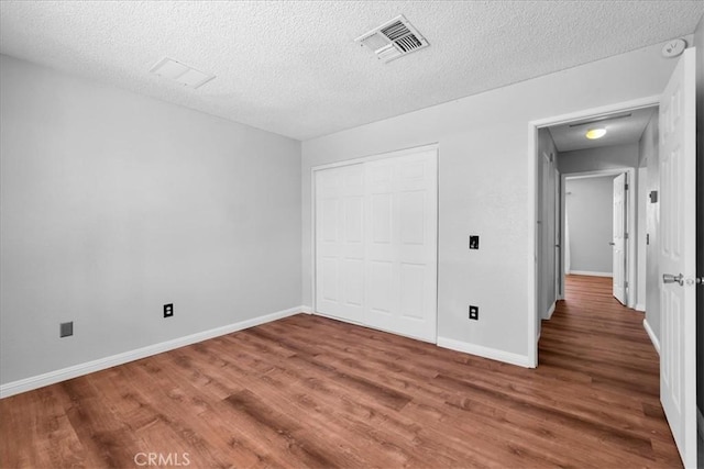unfurnished bedroom featuring a closet, a textured ceiling, baseboards, visible vents, and wood finished floors