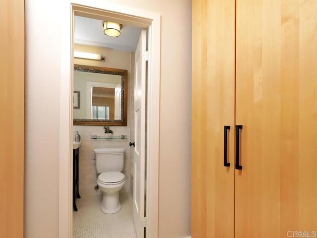 half bath with toilet, tile walls, and tile patterned floors