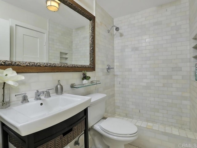 bathroom featuring toilet, a tile shower, tile walls, decorative backsplash, and vanity