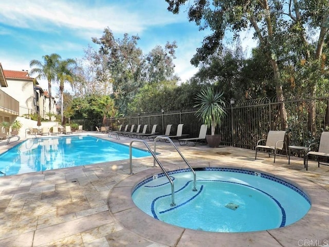 community pool with a patio area, a community hot tub, and fence