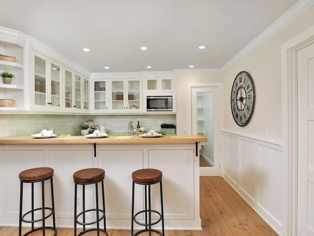 kitchen featuring white cabinetry, a breakfast bar, light wood finished floors, and stainless steel microwave