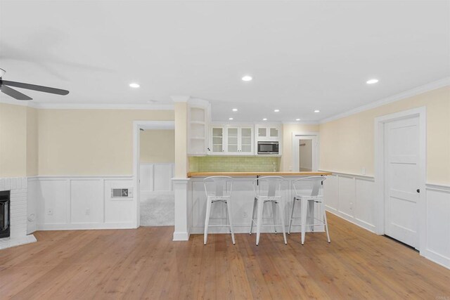 3527 Caminito Sierra Unit 202, Carlsbad, CA 92009 - kitchen with stainless steel microwave, a breakfast bar, white cabinets, light wood-type flooring, and a wainscoted wall