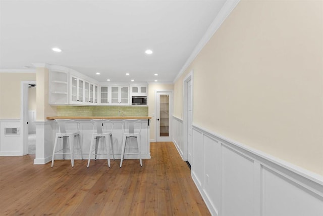 3527 Caminito Sierra Unit 202, Carlsbad, CA 92009 - kitchen with stainless steel microwave, ornamental molding, a wainscoted wall, white cabinets, and a breakfast bar