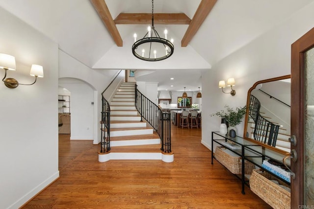 entrance foyer with a chandelier, stairs, beamed ceiling, and arched walkways
