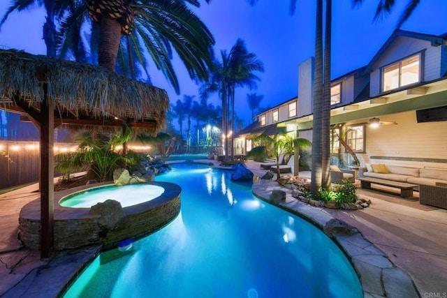 pool at twilight featuring a pool with connected hot tub, ceiling fan, a patio, and outdoor lounge area