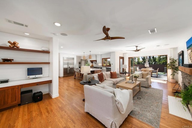 living room with light wood-style floors, visible vents, and ceiling fan