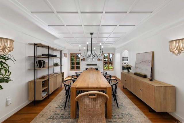 dining space featuring coffered ceiling, a fireplace, dark wood finished floors, baseboards, and a chandelier
