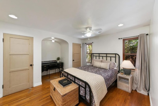 bedroom with arched walkways, multiple windows, light wood-style flooring, and recessed lighting