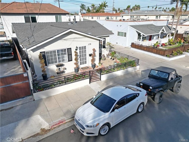 view of front of house with a fenced front yard, stucco siding, a residential view, roof with shingles, and a gate