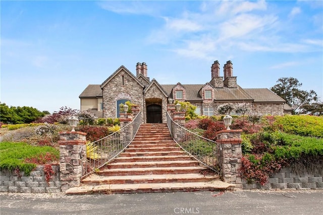 view of front of property featuring stone siding, stairway, and a chimney