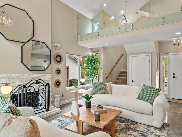 living area featuring high vaulted ceiling, stairway, baseboards, a chandelier, and a fireplace with raised hearth
